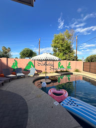 Scottsdale backyard pool with scalloped umbrella, lounge chairs, pink wall cactus mural, heart-shaped float and clear blue sky
