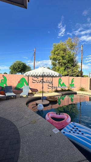 Scottsdale backyard pool with scalloped umbrella, lounge chairs, pink wall cactus mural, heart-shaped float and clear blue sky
