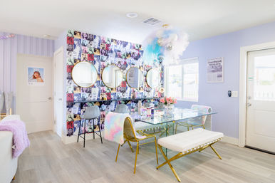 Bright pastel beauty studio interior with pop-art collage wall, three round vanity mirrors, glass communal table, gold-framed chairs and bench, fluffy pastel throws and a whimsical balloon-and-tulle chandelier