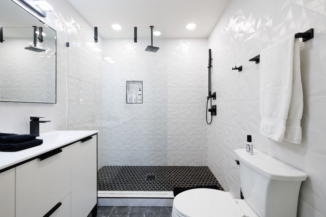 Bright contemporary white bathroom with frameless glass walk-in shower, black hexagon floor tiles, matte-black fixtures, white vanity and towel rack