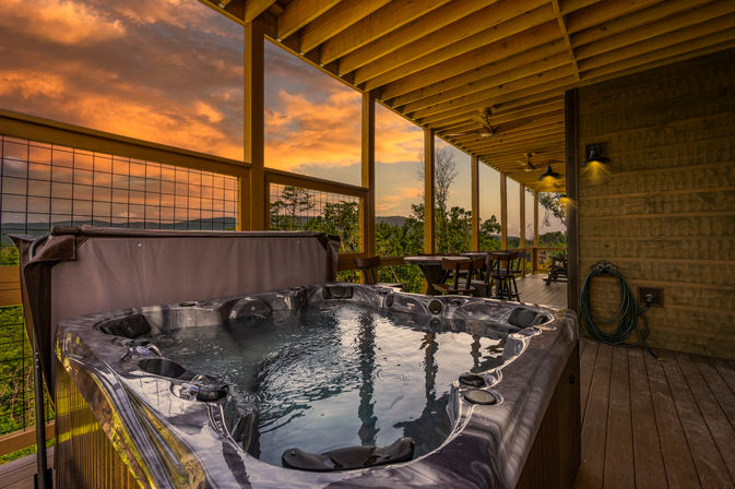 Cozy hot tub on a covered wooden mountain-cabin deck with outdoor seating and panoramic sunset views.