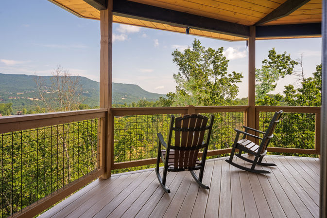 Covered wooden deck with two rocking chairs overlooking a lush forest and distant mountain views, scenic porch perfect for relaxing
