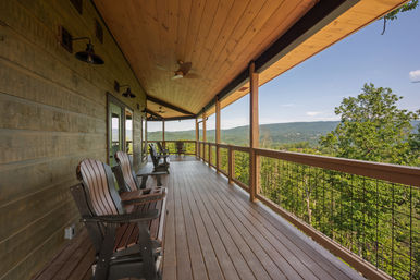 Covered wooden mountain porch with Adirondack chairs and ceiling fans overlooking a panoramic green forested valley and distant rolling mountains