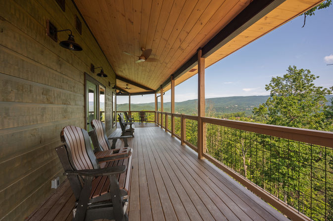 Covered wooden mountain porch with Adirondack chairs and ceiling fans overlooking a panoramic green forested valley and distant rolling mountains