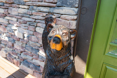 Friendly wooden bear carving waving at a front porch entrance beside a stacked stone wall and bright green door.
