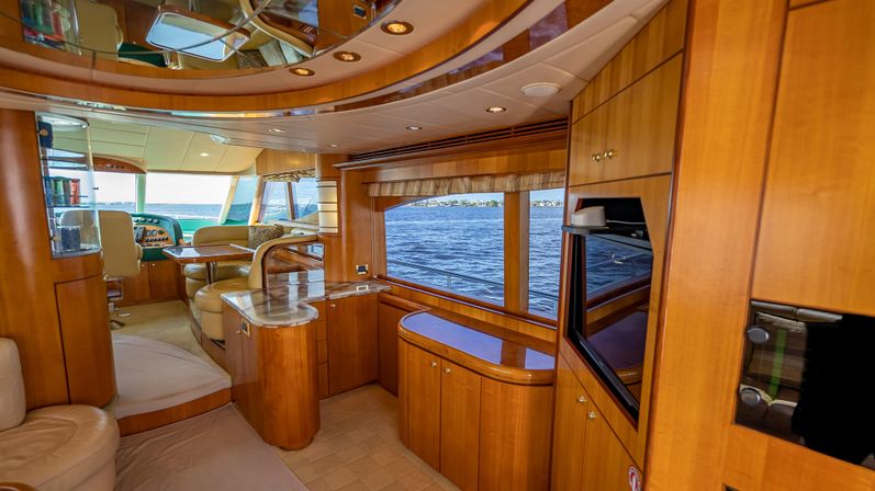 Luxurious wood-paneled yacht interior with curved cabinetry, leather seating and helm station, large windows revealing a panoramic blue water view.