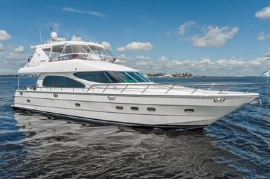 Sleek white luxury motor yacht gliding across sparkling coastal waters under a sunny blue sky with a distant waterfront skyline.