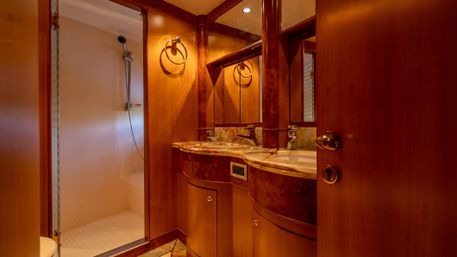 Warm wood-paneled luxury cabin bathroom with marble countertop and sink, mirrored vanity, round towel ring and compact shower stall
