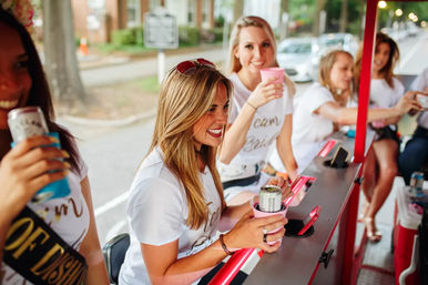 Bachelorette party friends in matching 'Team Bride' shirts smiling and holding canned drinks on an outdoor party trolley.