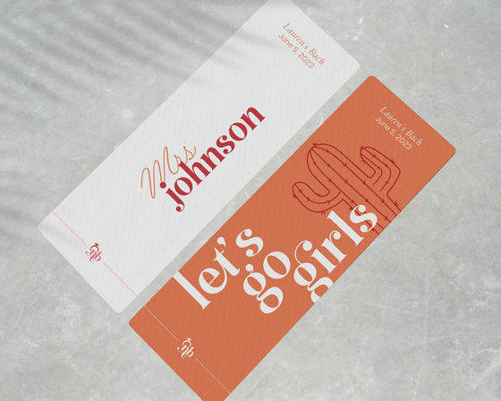Two angled bachelorette-style tickets on a gray stone background — a white name card in red script and a terracotta ticket with bold white "let's go girls" text and a cactus illustration.