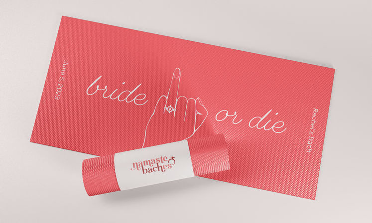 Pink textured yoga mat printed with cursive “bride or die” and a line-drawn hand flashing the middle finger with a ring; a matching rolled mat wrapped in a white paper band, playful bachelorette/bridal shower yoga gift.