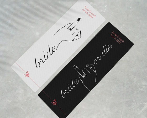 Two diagonal black and white bachelorette party cards on a marble surface, minimalist script “bride” design with a playful line-art hand flipping the middle finger wearing an engagement ring — sassy bridal shower keepsake