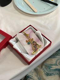 Gold-edged floral enamel cat keychain with small bead charms nestled in a red satin-lined gift box on a white craft table.