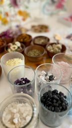 Close-up of assorted tumbled crystals, pink and white bath salts, and dried herbs in glass and wooden bowls on a wellness table
