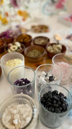 Close-up of assorted tumbled crystals, pink and white bath salts, and dried herbs in glass and wooden bowls on a wellness table