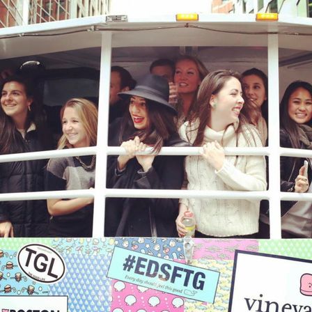Smiling group of young women leaning out of the window of a colorful city trolley during a lively downtown sightseeing ride