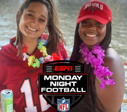 Two smiling women on a waterfront boat wearing Tampa Bay Buccaneers gear and colorful leis, one holding a canned drink, with an ESPN Monday Night Football logo overlaid.
