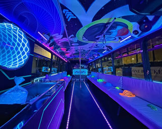Neon-lit party bus interior at night with long bench seating, center dance pole, LED floor strips, DJ booth and a colorful cosmic ceiling mural with blacklight-glowing hats.