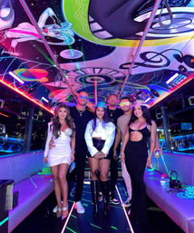 Six friends posing inside a neon-lit party bus with a colorful cosmic mural ceiling, LED strip lights, poles and lounge seating — vibrant nightlife party vibe.