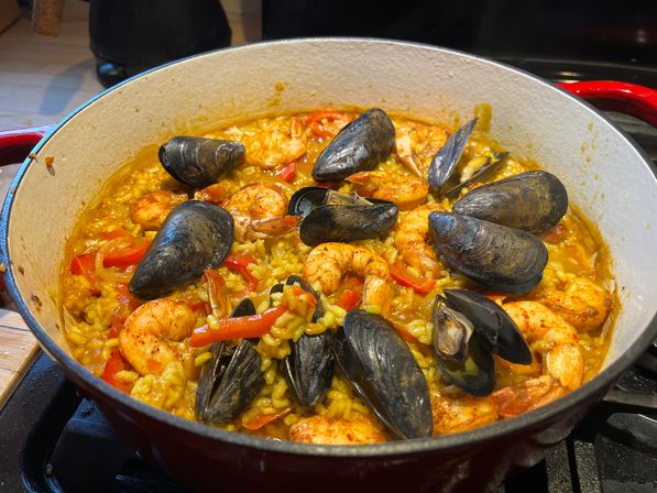 Spanish-style seafood paella in a red enameled Dutch oven: saffron-yellow rice with shrimp, mussels and red bell pepper on a stovetop