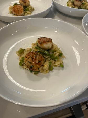 Two golden seared scallops on creamy asparagus risotto with chopped asparagus and herbs, plated in a white shallow bowl