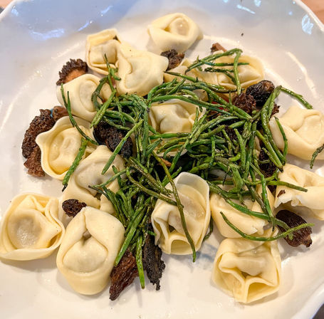 Tortellini pasta dish topped with vibrant sea asparagus (samphire) and sautéed wild mushrooms on a white plate