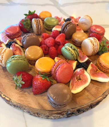 Vibrant dessert platter of colorful macarons with strawberries, raspberries, figs and blackberries arranged on a round wooden serving board — bright brunch or event treat