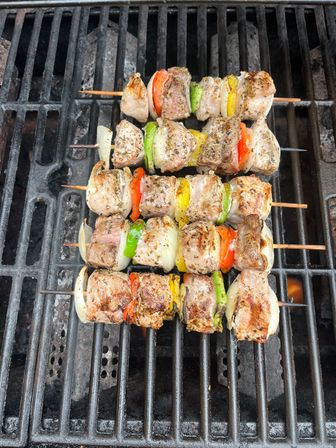 Juicy seasoned chicken kebabs on skewers with red, yellow and green bell peppers and onion slices cooking on an outdoor barbecue grill over hot grates.