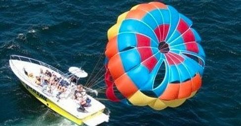 Colorful rainbow parasail canopy pulled by a white speedboat across deep blue ocean, passengers enjoying parasailing water sport