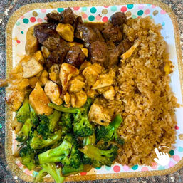 Hibachi-style takeout plate with grilled steak cubes, teriyaki chicken bites, sautéed broccoli and golden fried rice on a colorful paper tray.