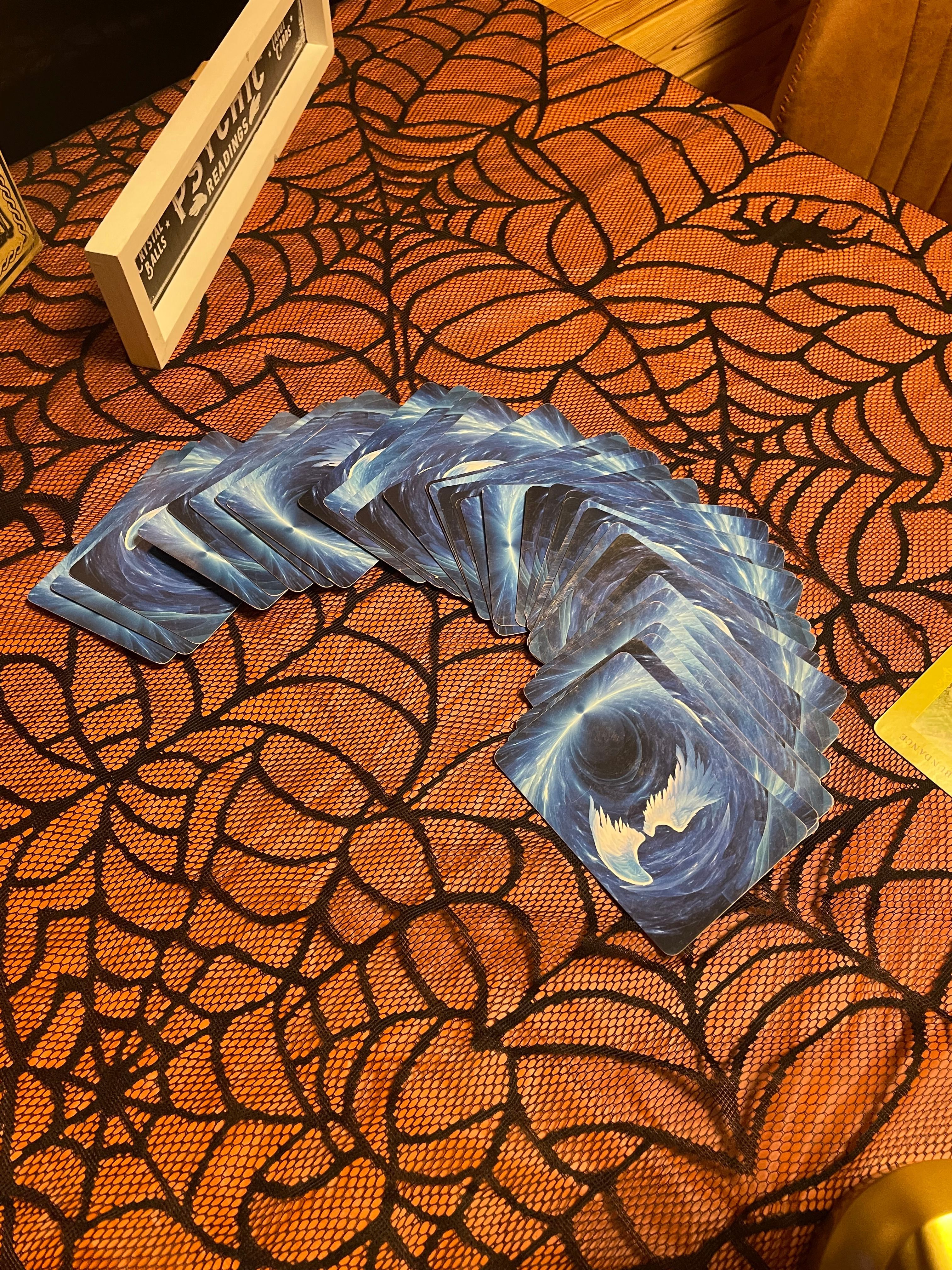 Fanned blue cosmic-back tarot cards arranged for a reading on an orange spiderweb Halloween tablecloth.