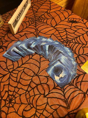 Fanned blue cosmic-back tarot cards arranged for a reading on an orange spiderweb Halloween tablecloth.