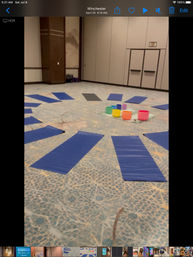 Blue yoga mats arranged in a circle on a patterned carpet inside a conference room surrounding bright, colorful crystal singing bowls for a sound-healing yoga session