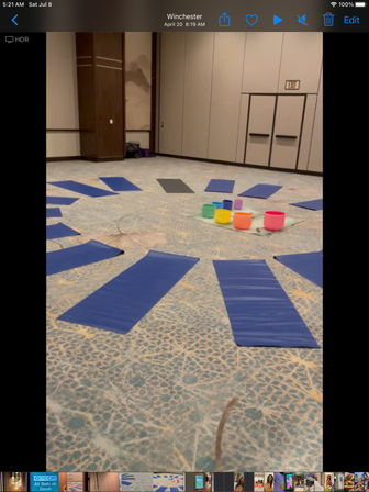 Blue yoga mats arranged in a circle on patterned carpet inside a conference room, colorful bowls placed in the center for a meditation or wellness workshop