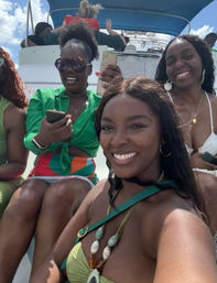 Four smiling women in colorful swimwear on a sunny boat cruise, blue sky overhead and a relaxed tropical-vacation vibe.