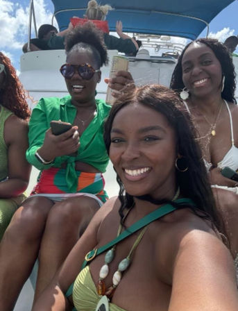 Four smiling women in colorful swimwear on a sunny boat cruise, blue sky overhead and a relaxed tropical-vacation vibe.
