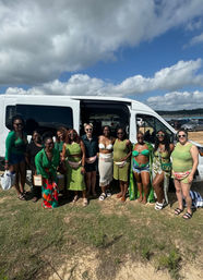 Group of women in green outfits posing in front of a white van at a sunny beach parking area under a blue sky — lively bachelorette outing