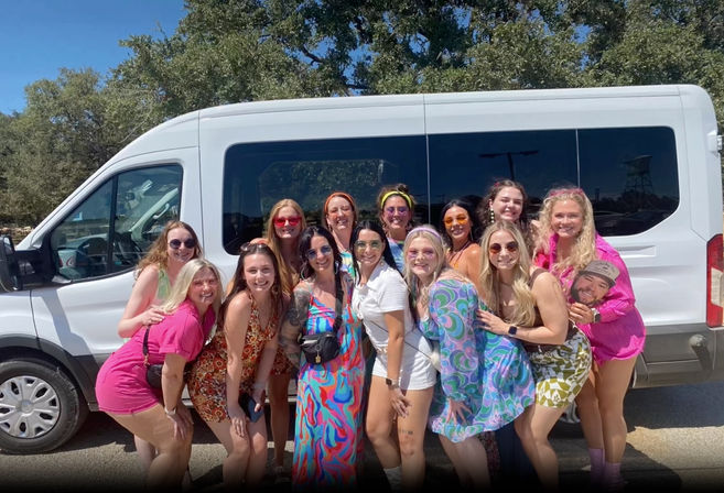 Group of women friends in colorful retro outfits smiling and posing in front of a white passenger van on a sunny outdoor parking lot