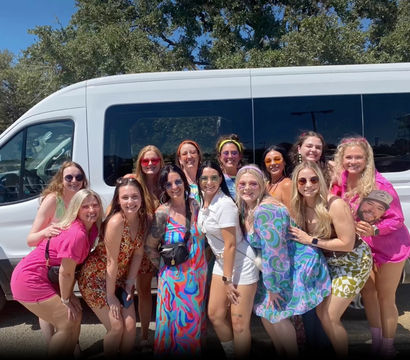 Group of women friends in colorful retro outfits smiling and posing in front of a white passenger van on a sunny outdoor parking lot
