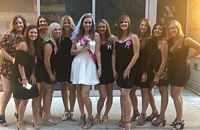 Bride in a short white dress and veil holding a bouquet posing with friends in black dresses outside a downtown venue for a bachelorette party