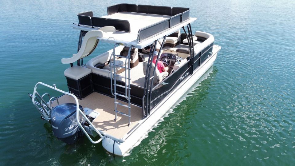 Leisure pontoon boat with rooftop lounge, water slide, swim ladder and outboard motor floating on a calm green lake