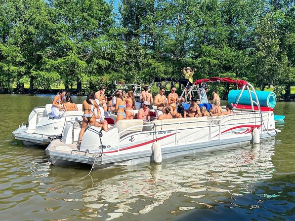 Sunny pontoon boat party on a calm, tree-lined river with a group of people in swimsuits, a blue inflatable tube and relaxed summer vibes.