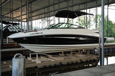 Sleek black-and-white motorboat suspended on a boat lift under a covered marina dock with a black bimini top and calm water reflections.