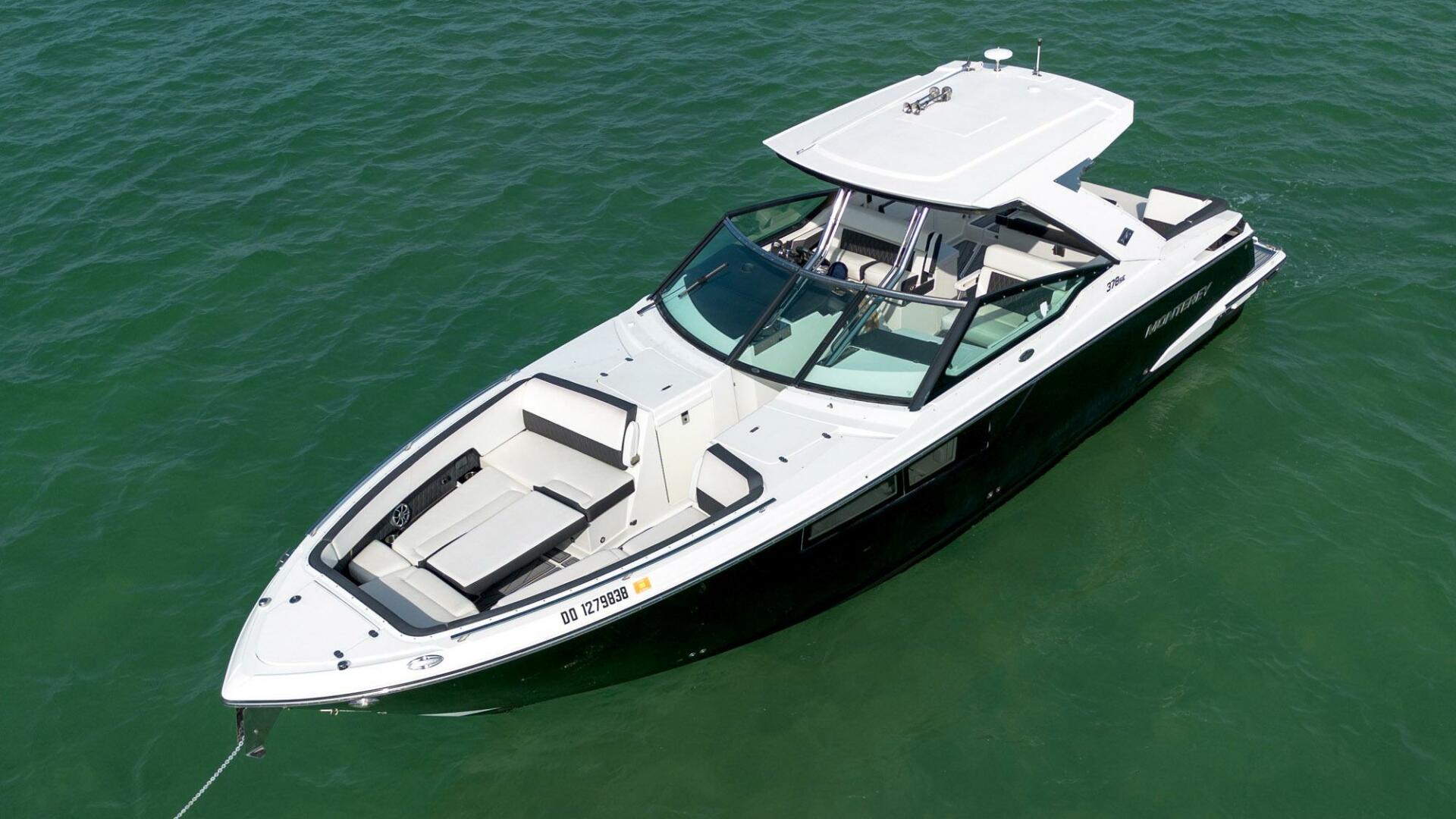 Overhead view of a sleek white-and-black motorboat anchored in emerald water, showing cushioned bow seating, wraparound windshield, covered helm and roomy cockpit—ready for a day on the water.