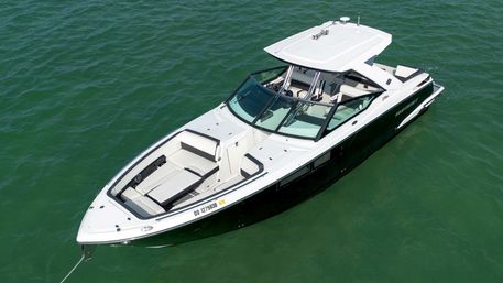 Overhead view of a sleek white-and-black motorboat anchored in emerald water, showing cushioned bow seating, wraparound windshield, covered helm and roomy cockpit—ready for a day on the water.