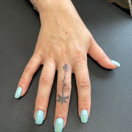 Close-up of a hand on black leather showing a tiny snowflake finger tattoo with a delicate line and pastel mint-green marbled nails