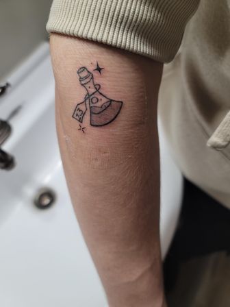 Small black-ink minimalist axe tattoo with a '13' tag and tiny sparkles on the inner forearm