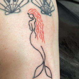 Minimalist mermaid outline tattoo in black linework with wavy red hair and shell accents on the forearm