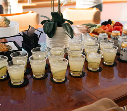 Sunlit yacht deck table in Cabo San Lucas with rows of salted-rim margaritas, canned beers, a fruit platter and orchid centerpiece.