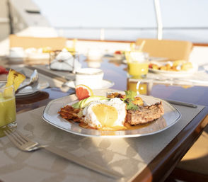 Sunlit luxury yacht breakfast: steak and eggs with avocado, crispy potatoes, grapefruit slice and green juice on a glossy deck table with ocean view